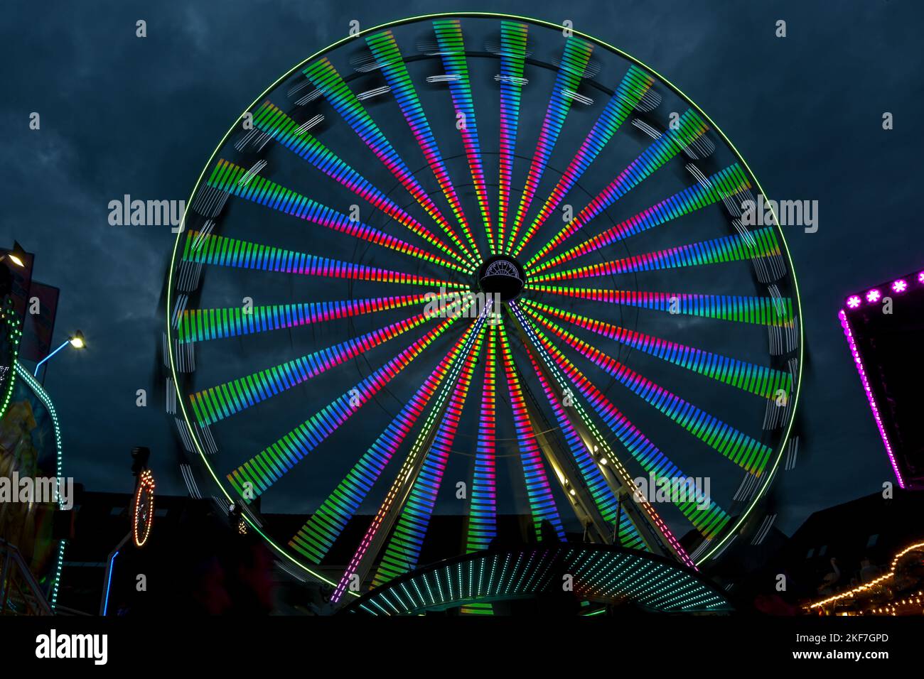 Lunga esposizione di una ruota gigante in movimento con luci colorate in una fiera di natale contro un cielo nuvoloso notte, immagine astratta, sfocatura del movimento Foto Stock