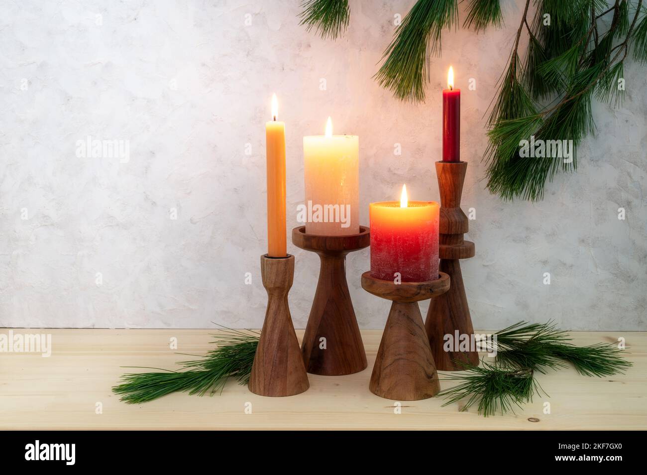 Quattro candele su stand di legno, tutte illuminate per il quarto Avvento, decorazione di rami di pino, asse di legno chiaro e sfondo rustico in gesso, spazio copia Foto Stock