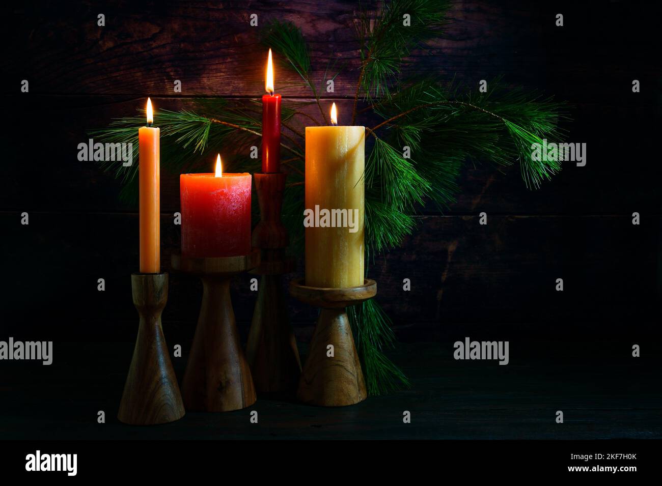 Disposizione dell'Avvento con quattro candele in rosso e giallo su supporti di legno e rami di pino su uno sfondo molto scuro di legno rustico, copia spazio Foto Stock