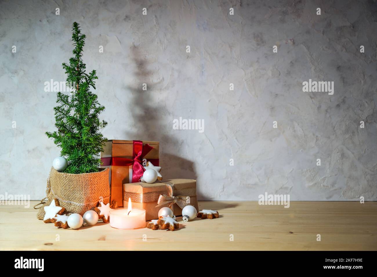 Alternativa bilancio albero di Natale, piccola pianta di conifere in vaso, decorato con stelle, baubles, regali e una candela su un tavolo di legno chiaro contro un rus Foto Stock