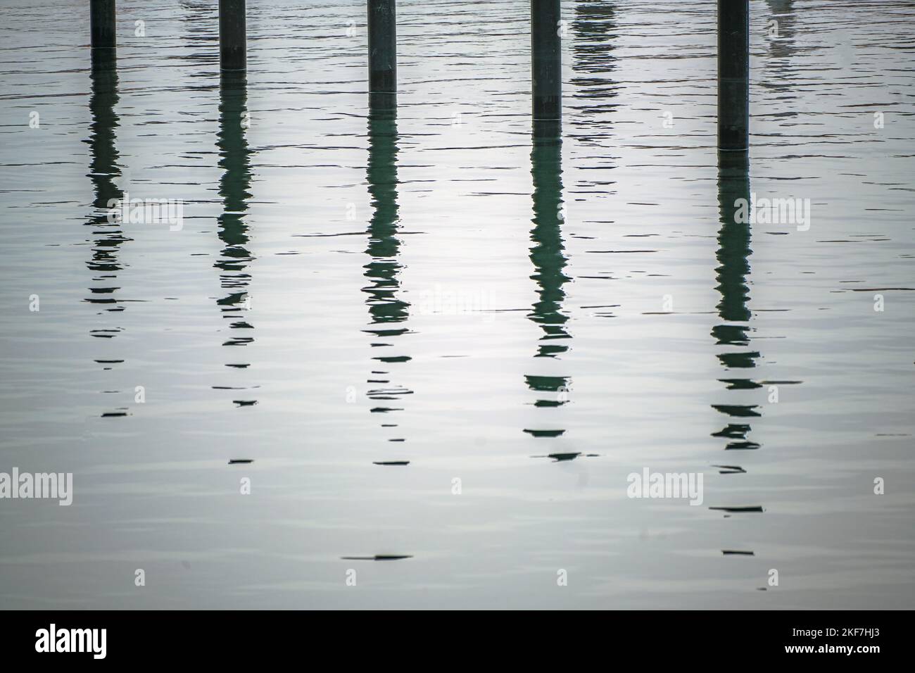 Palafitte o delfini ormeggi neri con riflessione in acqua in un porto turistico vuoto yacht sul Mar Baltico in un giorno grigio di novembre, immagine astratta, quasi Foto Stock