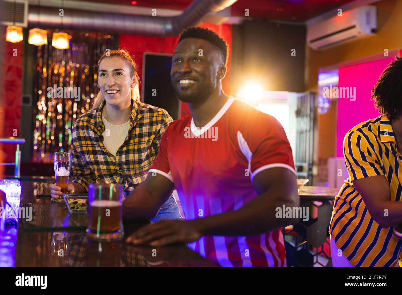 Amici maschili e femminili diversi ed eccitati che guardano le partite sportive in un bar Foto Stock