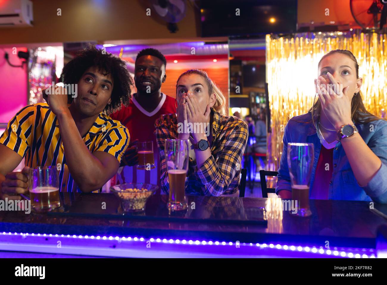 Quattro amici maschi e femmine, diversi e tesi, che guardano una partita di sport in un bar Foto Stock