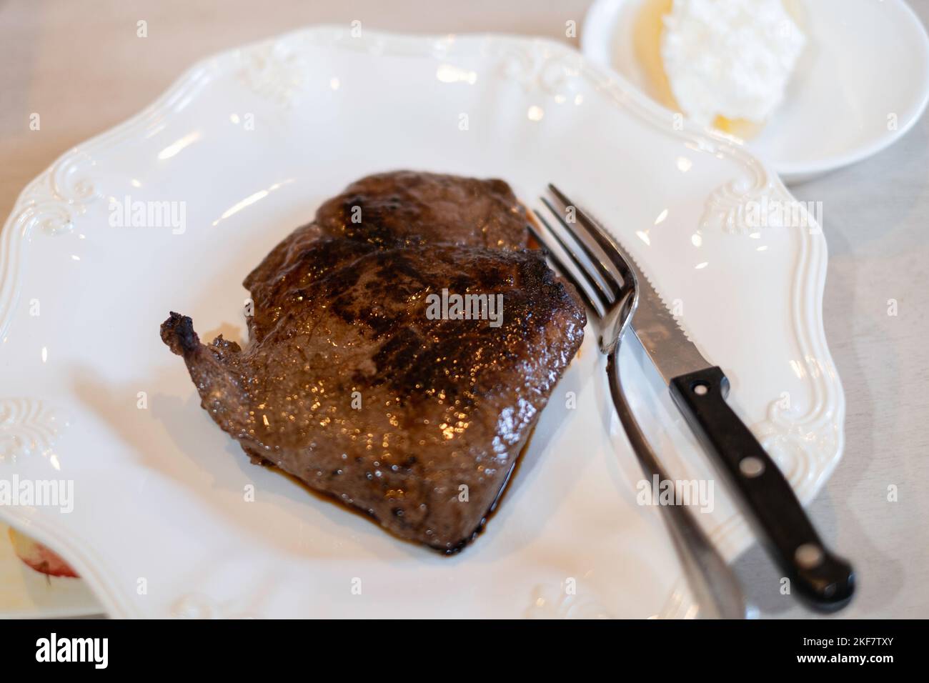 Bistecca di controfiletto alla griglia su un piatto bianco con utensili da cucina, un coltello e una forchetta. Foto Stock