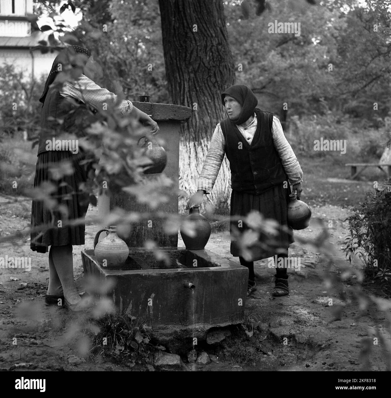 Contea di Teleorman, Repubblica socialista di Romania, circa 1973. Donne che riempiono le caraffe di ceramica con l'acqua di una fontana pubblica. Foto Stock