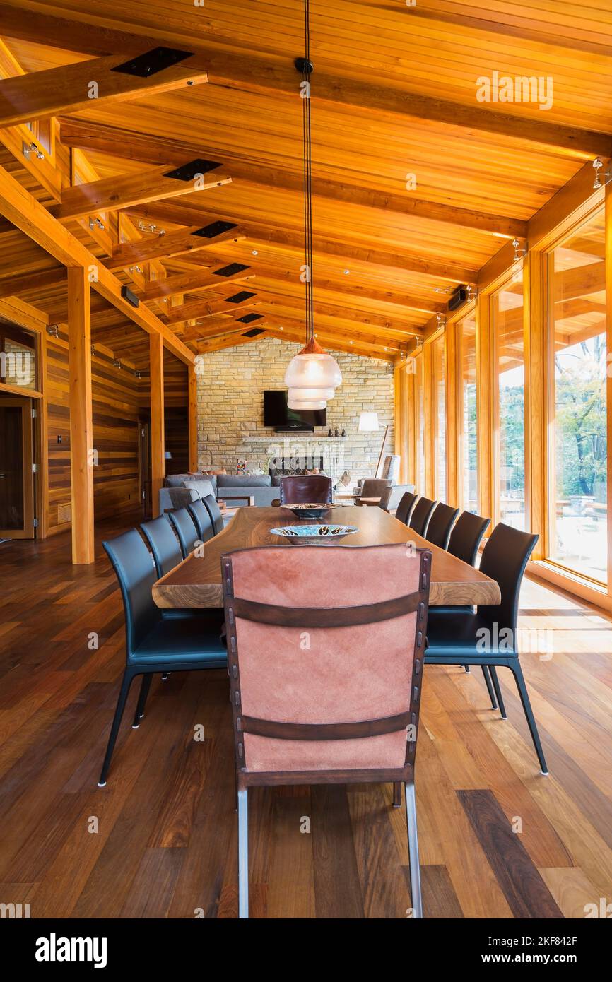 Tavolo da pranzo in legno con poltrone in rawhide, sedie in pelle nera e rame di stile industriale illuminato con lampade a sospensione in vetro smerigliato. Foto Stock