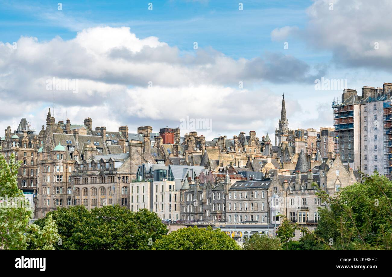 Splendidi edifici e tetti di Edimburgo New Town, visto da Princes Street Gardens, verdi alberi estivi in primo piano, cielo blu, soffici nuvole bianche, Foto Stock