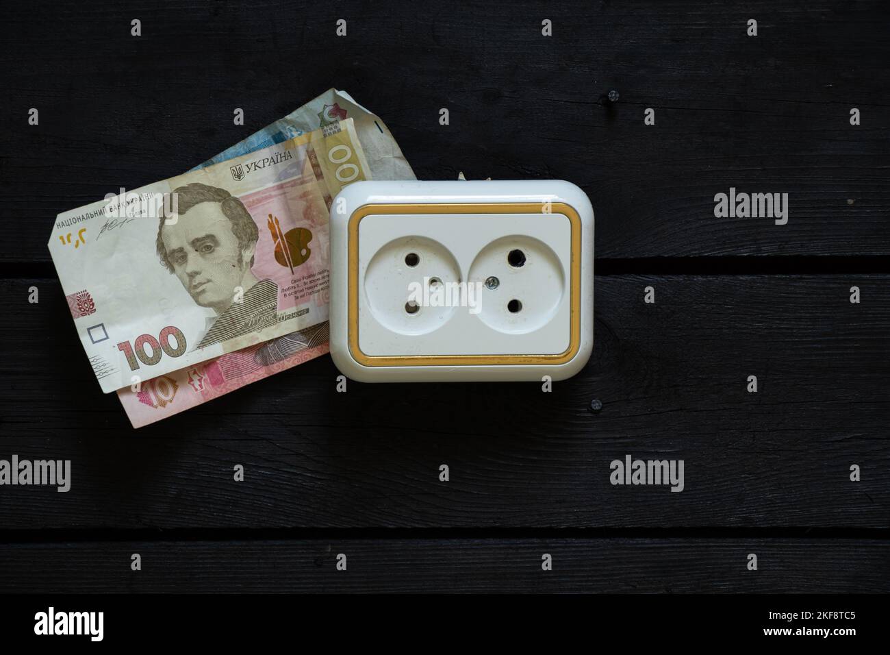 la plastica razetkana su un vecchio muro di legno e vicino a 100 hryvnia, aumento dei prezzi dell'elettricità, dei prezzi dell'elettricità, un altro aumento dei prezzi Foto Stock