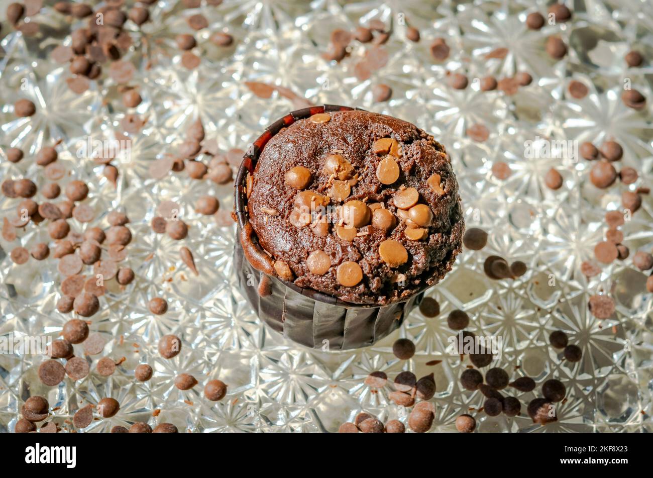 Un muffin fatto in casa con gocce di cioccolato sparse, macrofotografia ravvicinata, luce bianca del sole che splende da un lato. Messa a fuoco selettiva in primo piano. Foto Stock