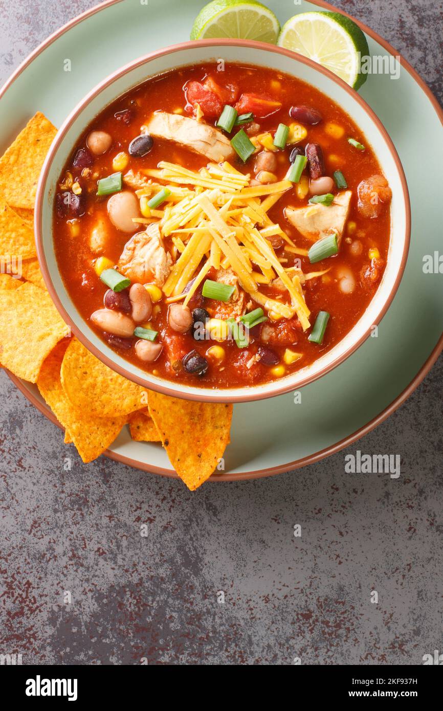 Zuppa messicana cremosa di taco di pollo con fagiolo nero, mais, pomodori, tortilla patatine sormontate con formaggio cheddar in un recipiente verde su un tavolo, verticale in cima vie Foto Stock
