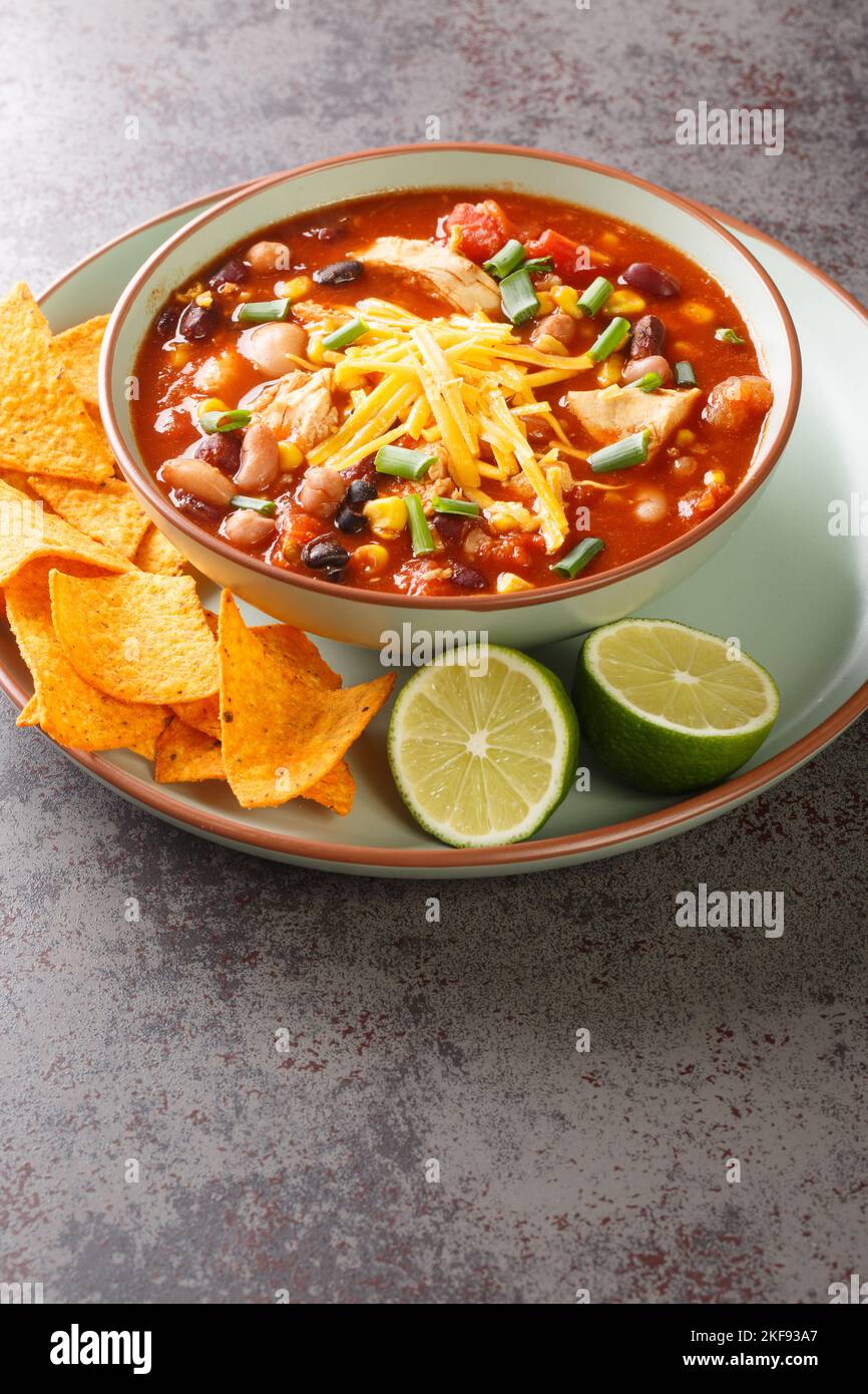 Abbondante zuppa di taco di pollo confezionata con fagioli neri, mais e pomodori con peperoncino verde primo piano in un piatto sul tavolo. Verticale Foto Stock