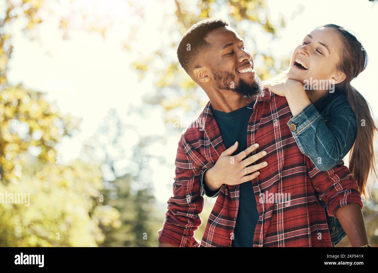 Coppia, abbraccio e sorriso mentre all'aperto con amore e cura nella natura, felice insieme mentre si legano nel parco. Uomo nero, donna e interracial, abbracciando dentro Foto Stock