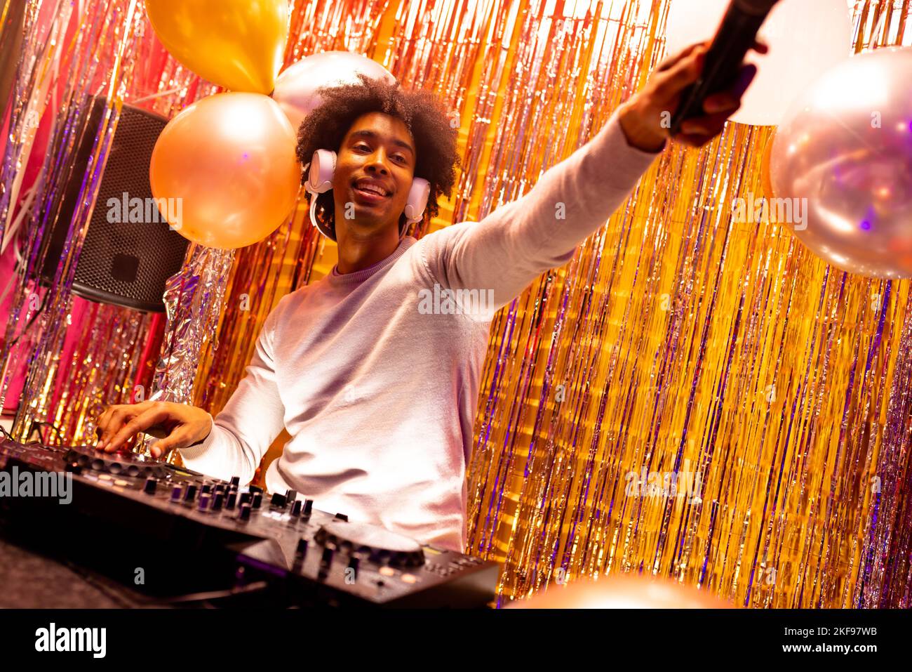 Sorridente dj afroamericano in cuffie che suonano musica in un nightclub e tengono il microfono Foto Stock