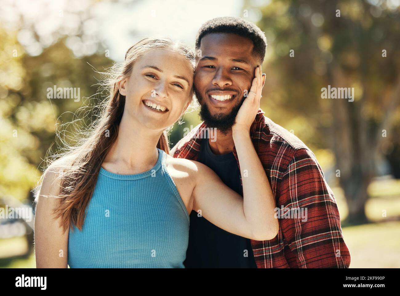 Ritratto di coppia interracial, giovani e rilassarsi nel parco, sole ed estate per amore, cura o tempo di qualità insieme. Uomo felice, donna sorridente Foto Stock