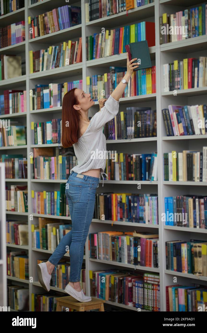 Giovane bibliotecario alla ricerca di un libro su scaffali Foto Stock