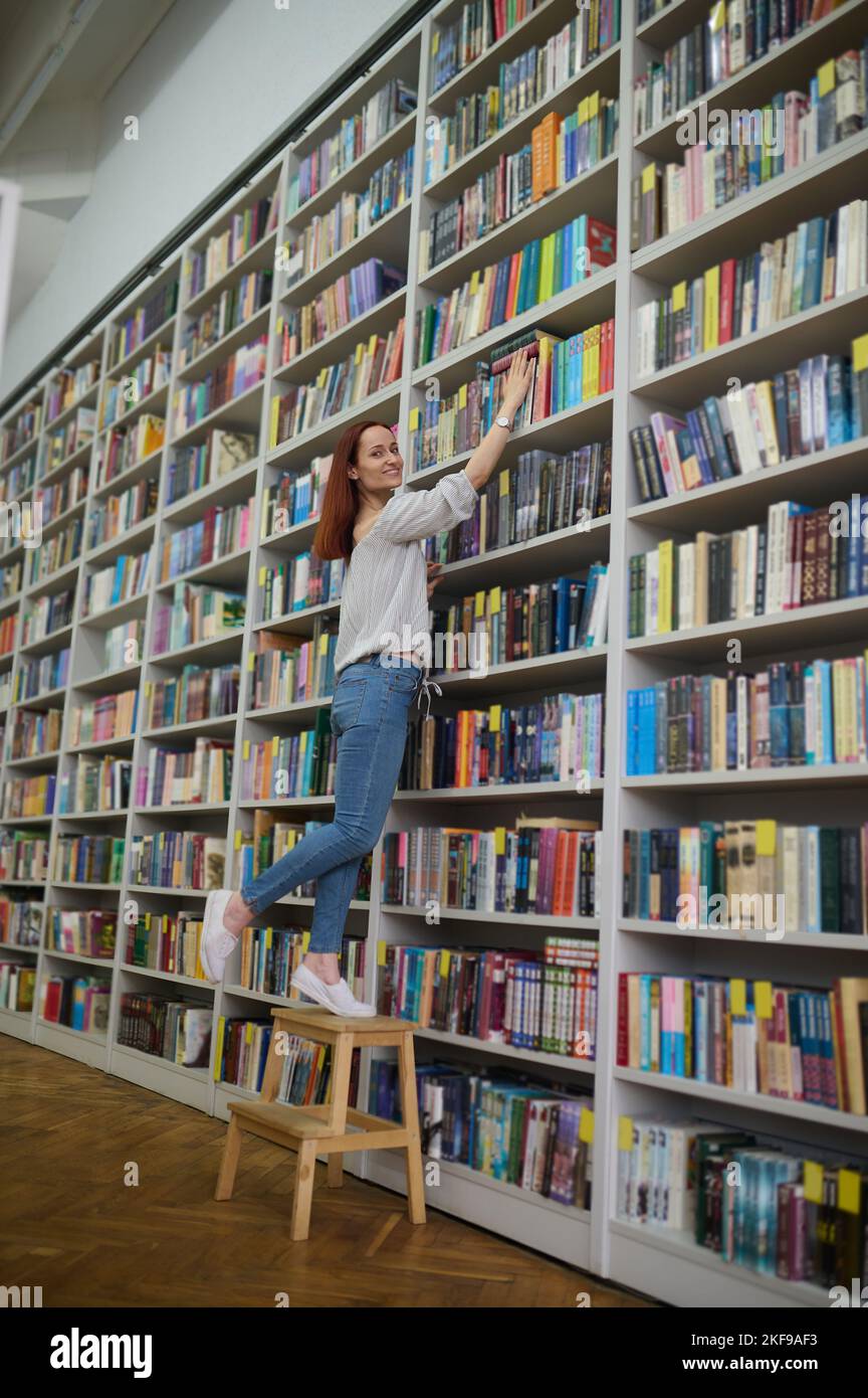 Giovane bibliotecario alla ricerca di un libro su scaffali Foto Stock