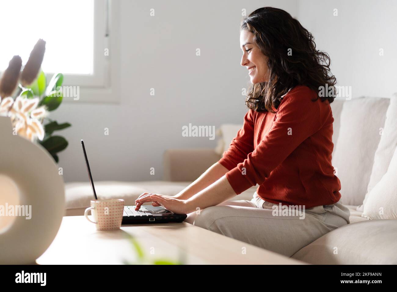 Una giovane donna felice che usa un computer portatile seduto sul divano a casa. Concetto di lavoro da casa Foto Stock
