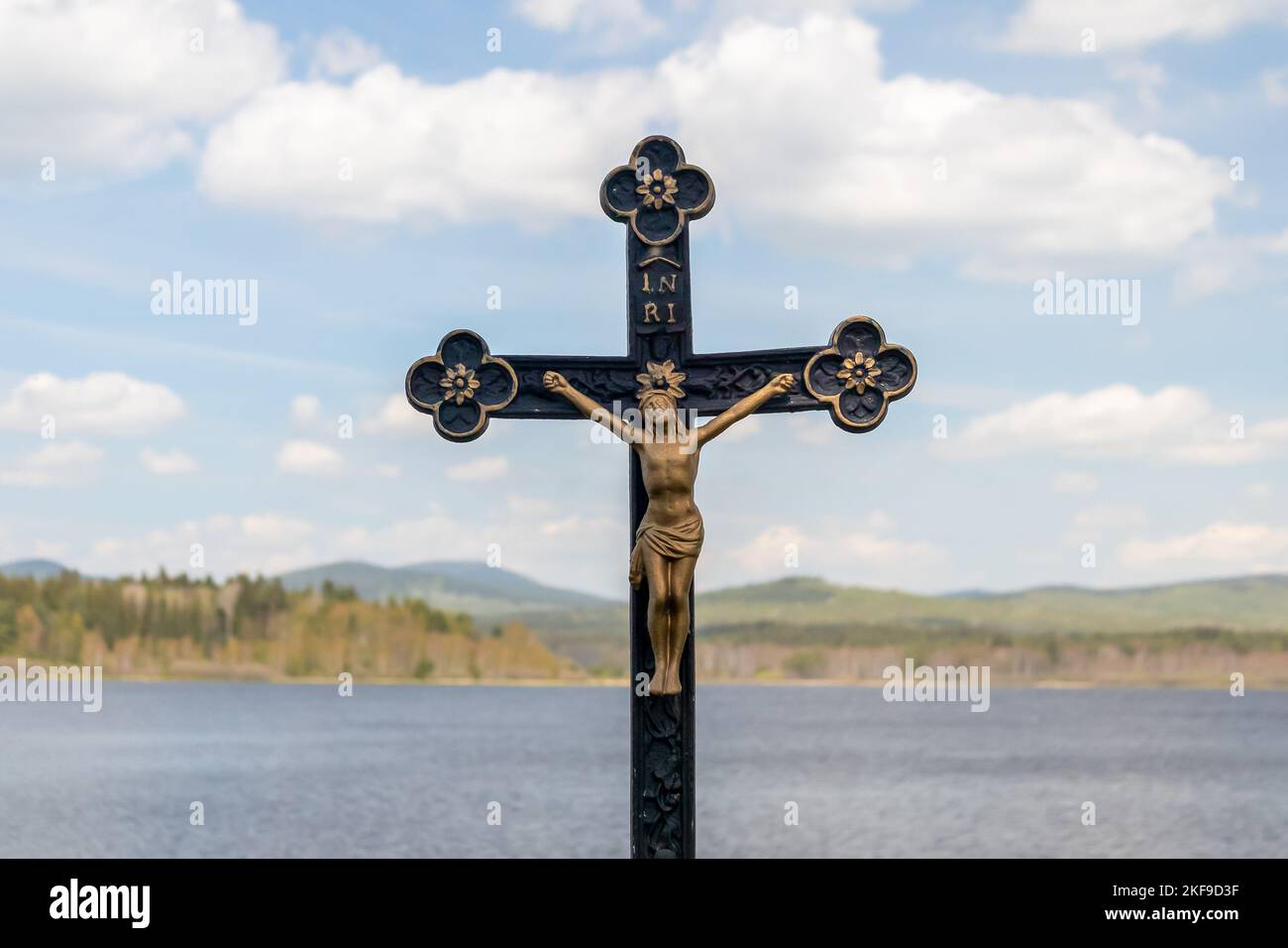 Crocifisso - statua di Gesù Cristo su una croce, sullo sfondo del paesaggio con acqua, colline e cielo blu con le nuvole Foto Stock