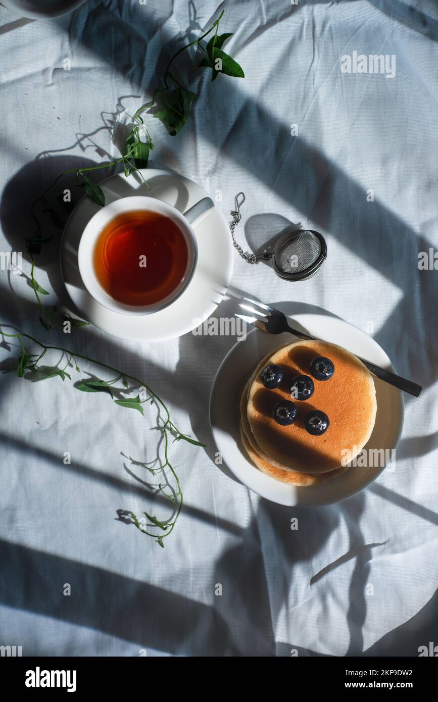 Pancake al mirtillo con tè, tovaglia bianca, spazio copia, shabby elegante piatto Foto Stock