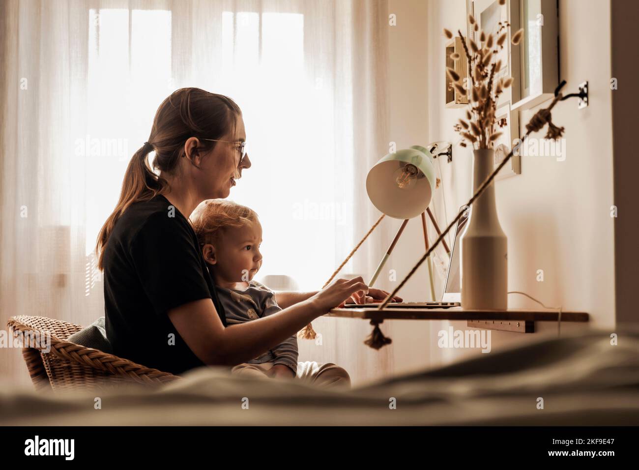 Donna occupata che lavora a casa con un bambino in grembo Foto Stock