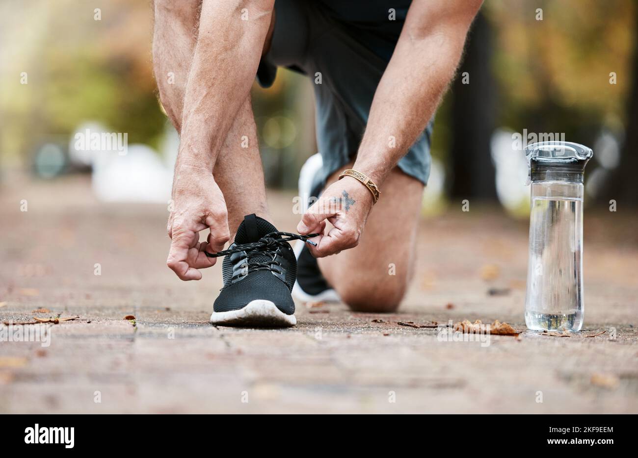 Fitness, ginnastica e scarpe da running mentre legano le scarpe a terra con bottiglia d'acqua per allenamento cardiovascolare o allenamento. Mani dell'uomo con le sneaker Foto Stock