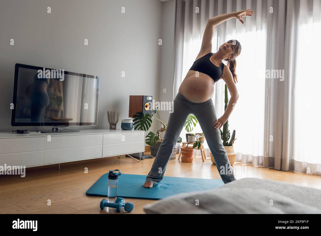 Donna incinta che si sta allenando a casa facendo esercizi di stretching. Mantenersi in buona forma mentre si aspetta il bambino Foto Stock