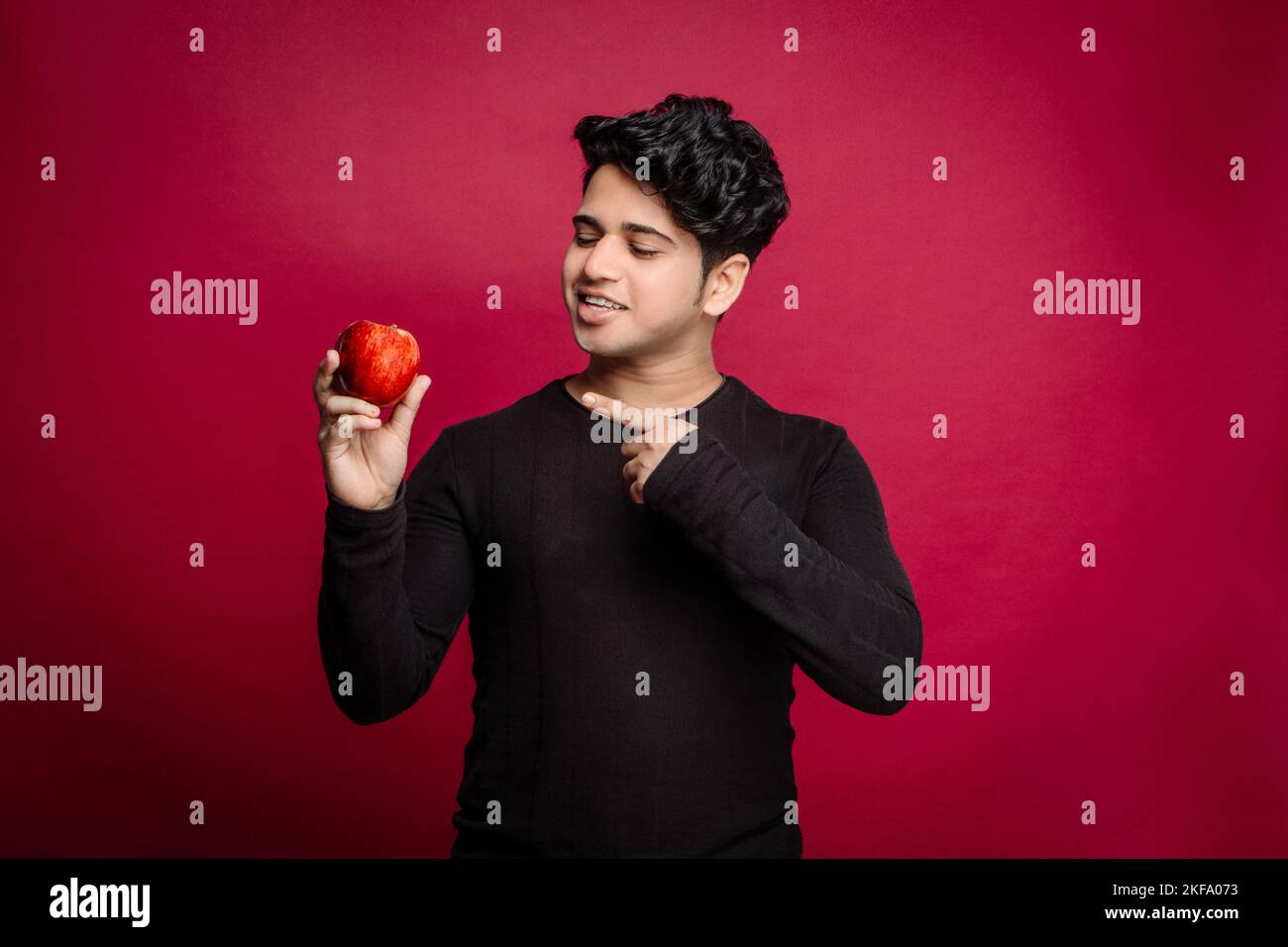 Giovane uomo indiano che promuove puntando le dita verso le mele fresche a scopo pubblicitario, ideale per le attività legate alle mele e le campagne di marketing Foto Stock