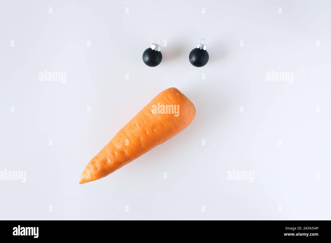 Pupazzo di neve creativo fatto di carote e palle di Natale su sfondo bianco. Concetto minimalista. Natale piatto Lay. Foto Stock