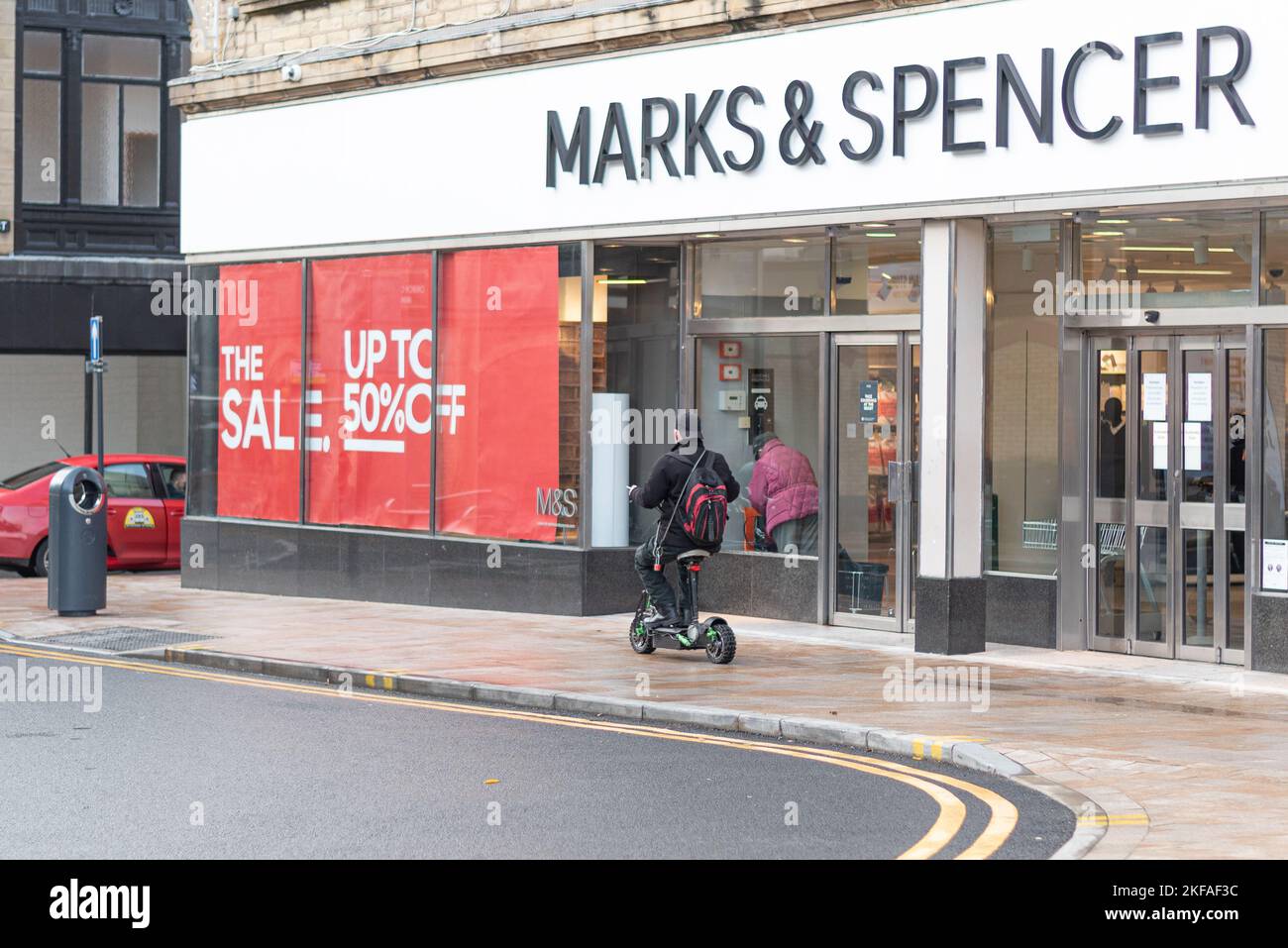 Uomo in sella a uno scooter elettrico sul marciapiede di fronte a Marks and Spencers nel centro di Burnley. Foto Stock