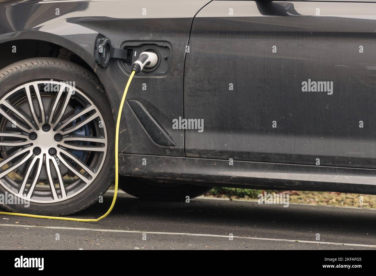 Auto ibrida nera parcheggiata sulla strada di guida in fase di ricarica con l'elettricità collegata. Foto Stock