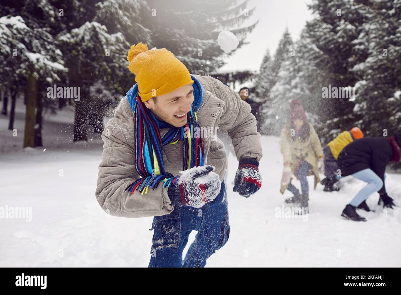 Giovane uomo allegro che ride a voce alta mentre gioca a palle di neve con gli amici nella foresta innevata. Foto Stock