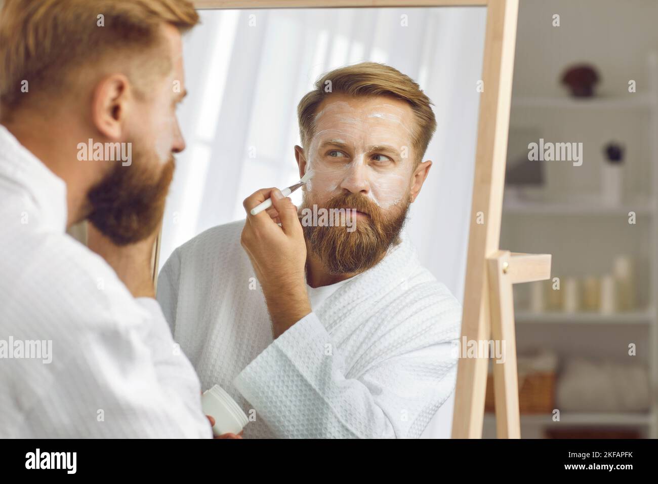 L'uomo adulto focalizzato che si prende cura della pelle con pennello applica crema idratante anti-invecchiamento. Foto Stock