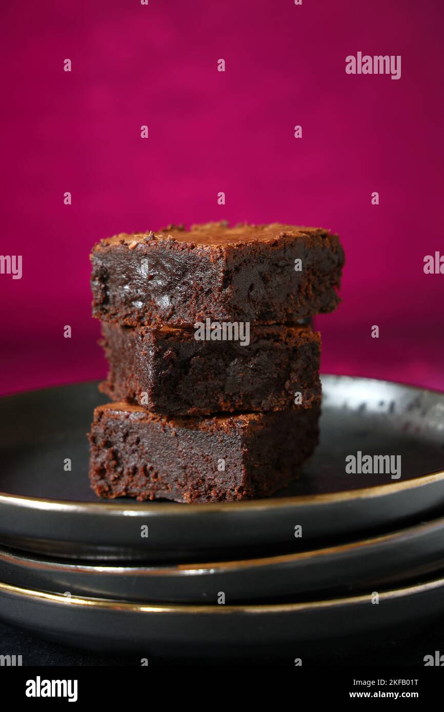 Una pila di brownie al cioccolato cotte in casa su uno sfondo rosa intenso, ideale per San Valentino Foto Stock