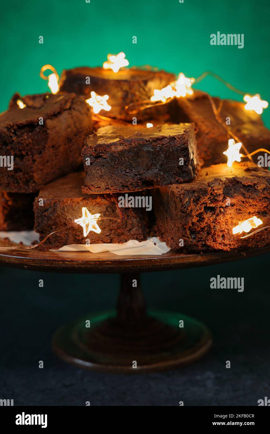 Una pila di brownie al cioccolato cotte in casa con luci stellari intrecciate su uno sfondo verde intenso e vivace con spazio copia Foto Stock