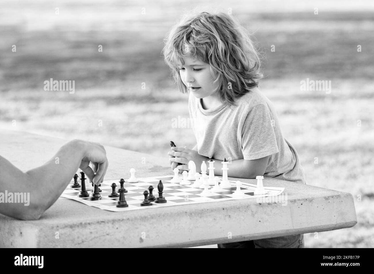 figlio bambino che gioca a scacchi sul tavolo nel parco all'aperto con suo padre, infanzia Foto Stock