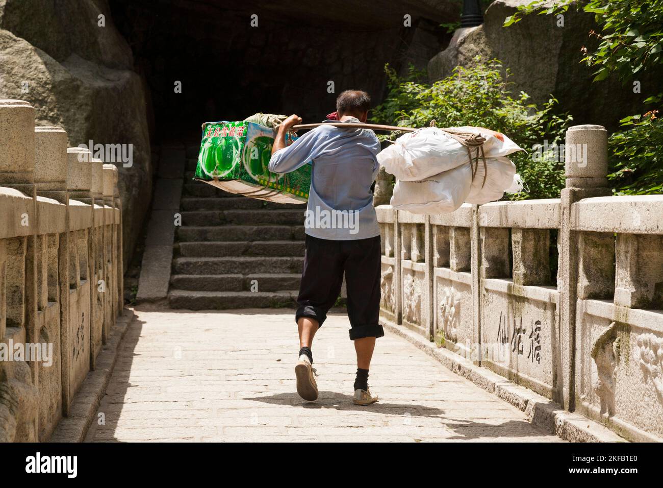 Uomo che lavora a Huashan Mountain / Monte Hua / Monte Hua vicino Huayin, Weinan, Cina. Egli trasporta / trasportando un carico pesante di forniture sul percorso / sentiero con l'aiuto di un bastone di trasporto palo. (125) Foto Stock