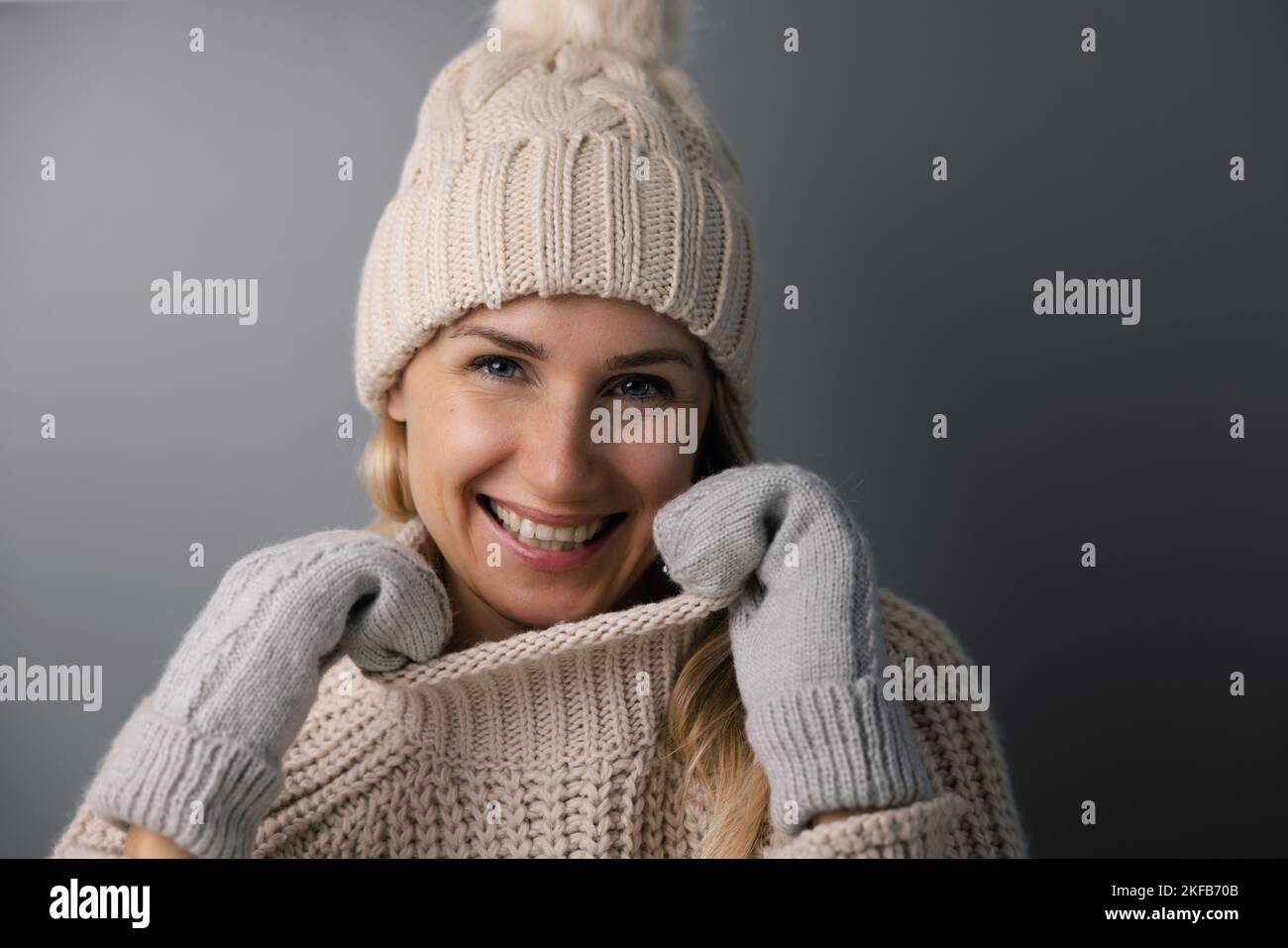 ritratto di donna sorridente in caldo abbigliamento invernale su sfondo grigio. vestiti di lana a maglia Foto Stock