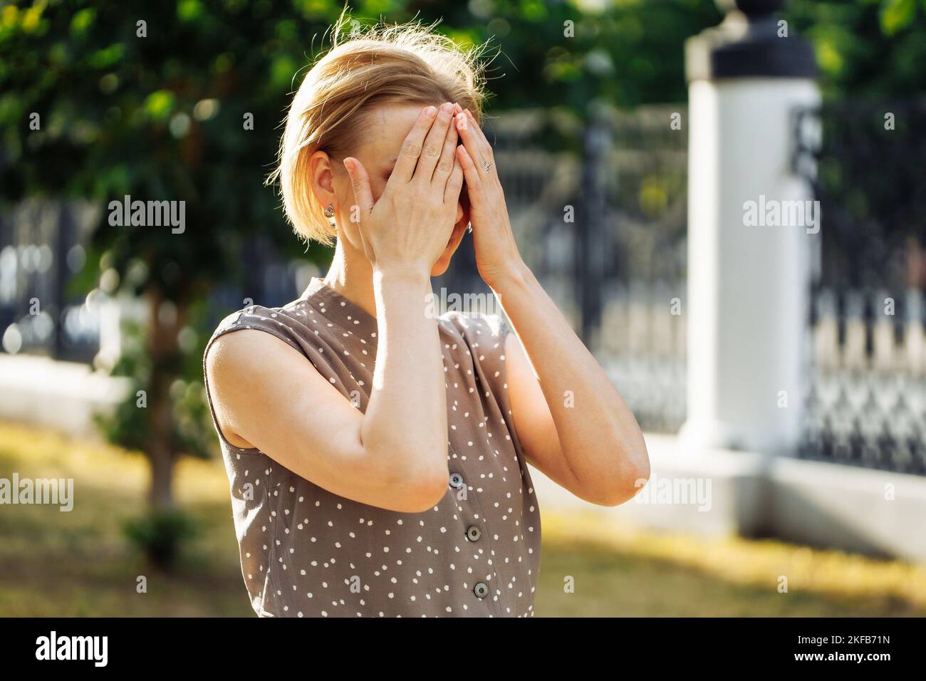 Ritratto di pensosa donna di 40 anni in piedi all'aperto tra alberi verdi in crescita in vicolo e mento toccante. Foto di donna di mezza età in giornata di sole Foto Stock