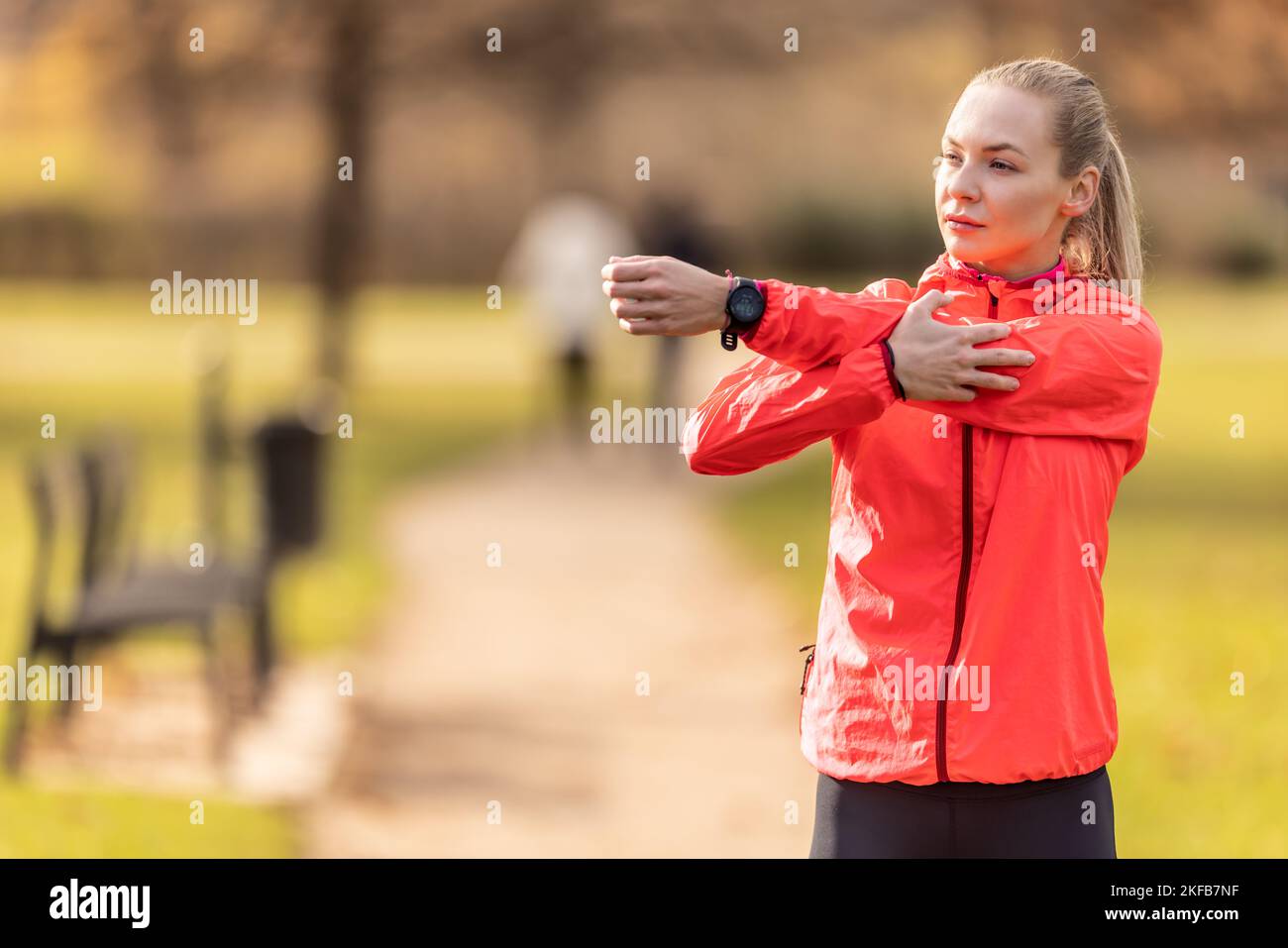Giovane donna che si scalda prima di fare jogging, facendo stretching del corpo superiore nel parco. Foto Stock