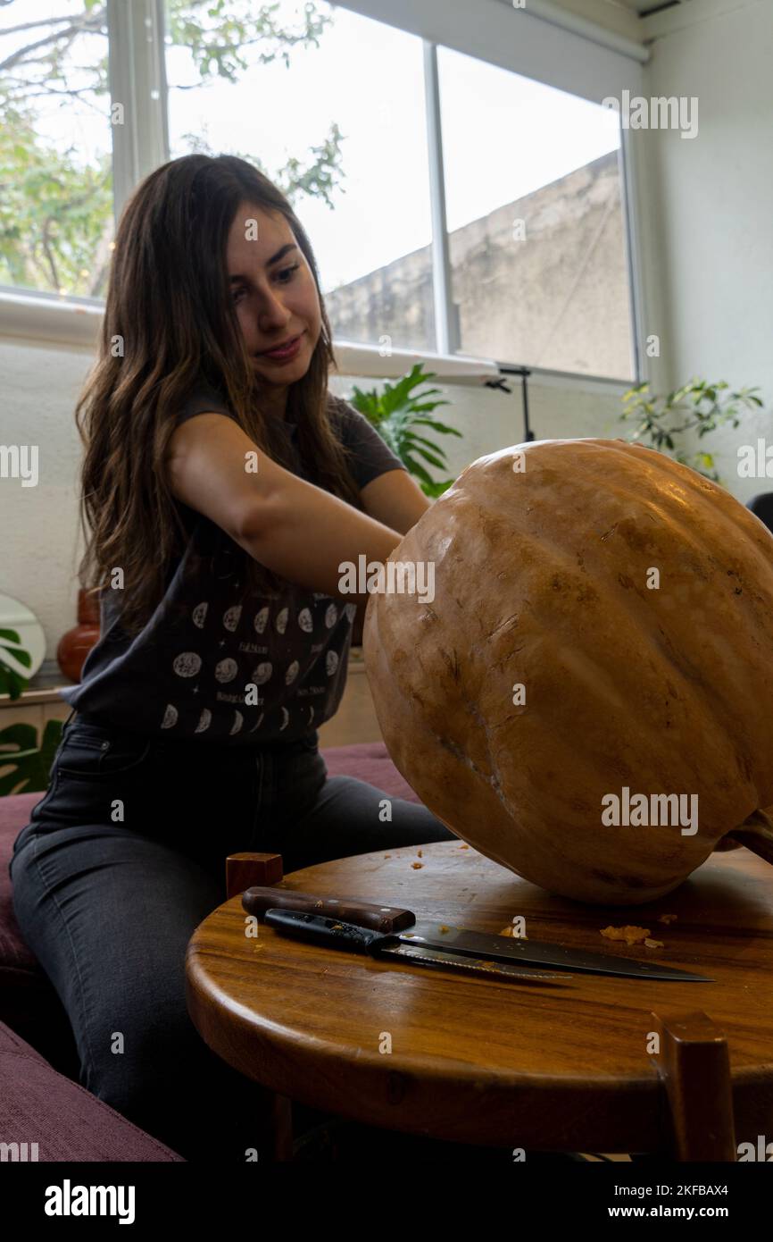 Femmina che intagliano grande zucca arancione per Halloween mentre seduto al tavolo di legno a casa Foto Stock