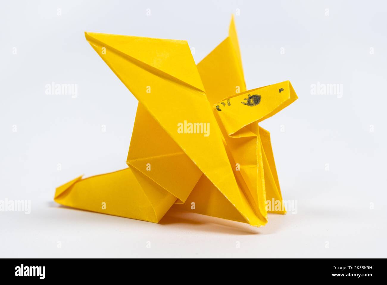 Origami drago carino giallo, una figurina animale di carta su sfondo bianco Foto Stock