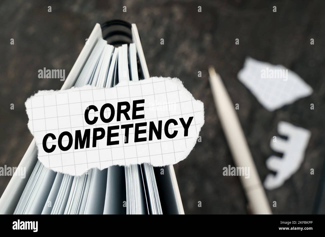Sul tavolo c'è un notebook su cui si trova un pezzo di carta strappata con l'iscrizione - Core Competency. La penna si trova al di fuori della zona di nitidezza. Foto Stock