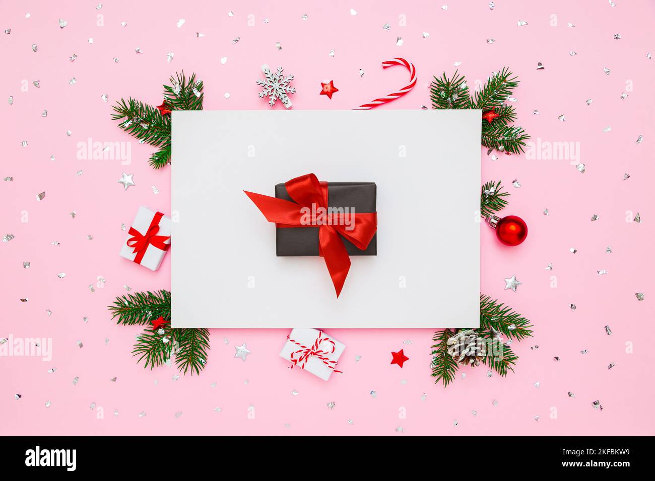 Natale, Capodanno disposizione vacanza. Scatola regalo nera con arco rosso in cornice di rami di abete naturale e decorazioni su piatto bianco e rosa pastello la Foto Stock