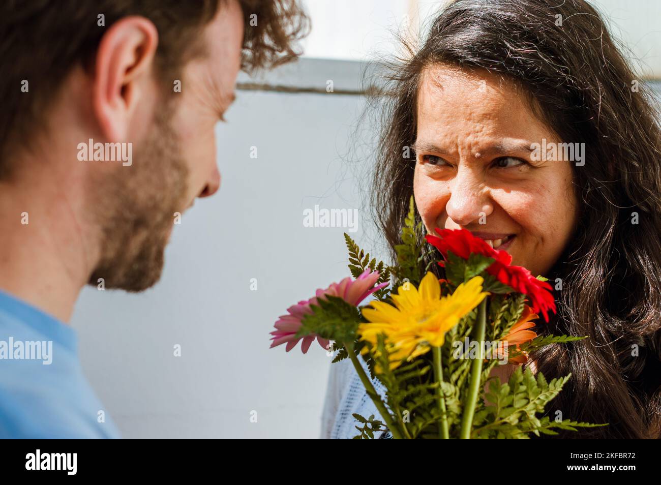 Donna brasiliana adulta a casa, sorridente, vede suo marito che le ha appena dato un bouquet di fiori colorati, celebrando il giorno di San Valentino. Foto Stock