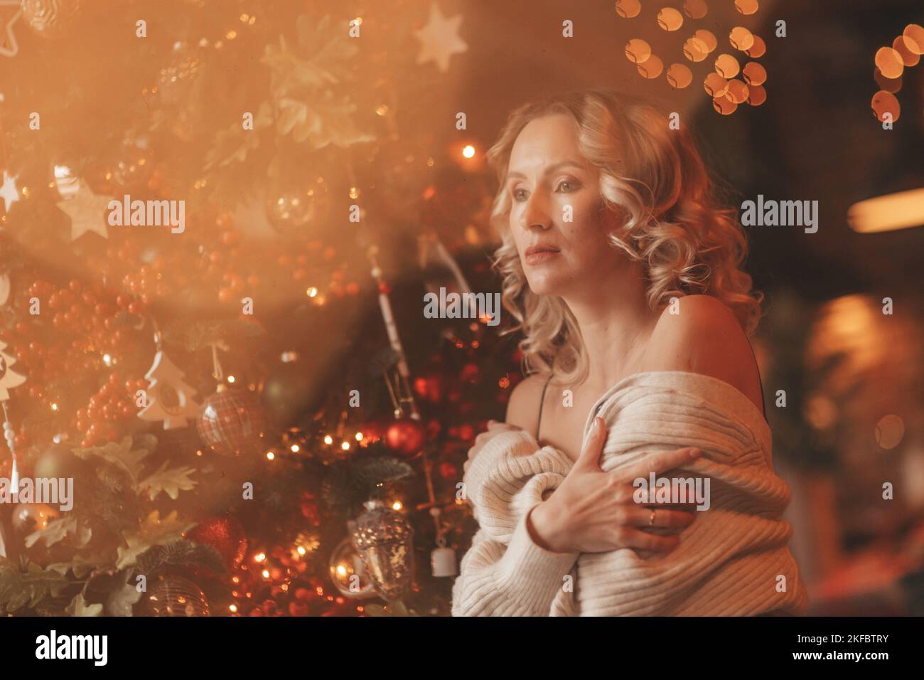 Ritratto di candido autentica donna bionda capelli ricci sognatore a casa chalet vigilia 25 dicembre vicino Noel albero bokeh luci. Donna in maglia vestito posa Foto Stock