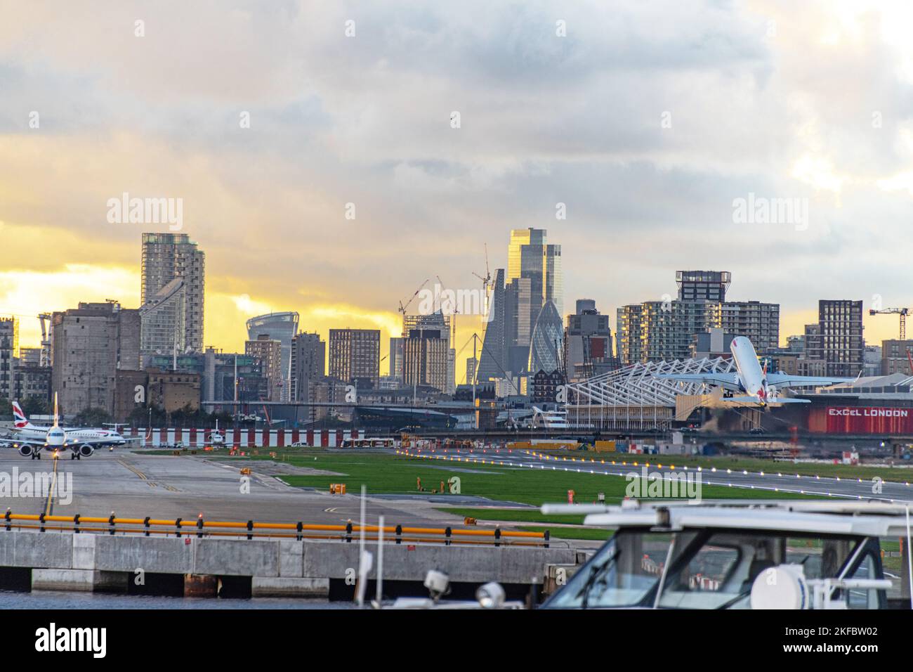 Un Embraer ERJ-190 della British Airways decoltra le nuvole scure all'aeroporto di London City con Canary Wharf sullo sfondo. Foto Stock