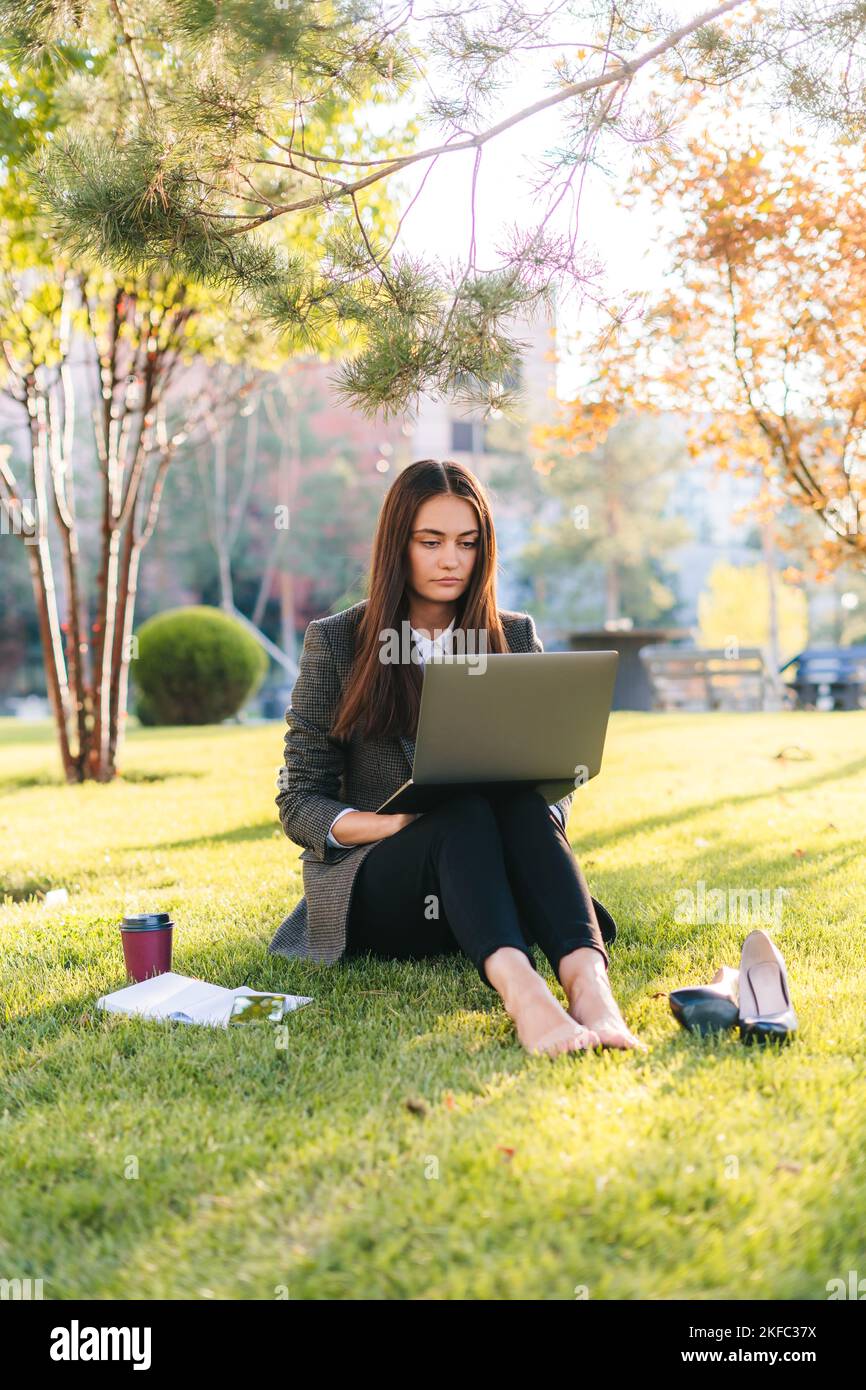 Una bruna donna penosa seduta nel parco sull'erba di fronte a un monitor di un notebook. Concetto di formazione online. Videochiamata in conferenza remota in linea Foto Stock