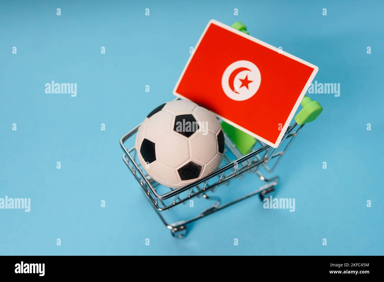 Pallone da calcio con bandiera tunisina nel carrello su sfondo blu. Guadagni della coppa di calcio. Foto Stock