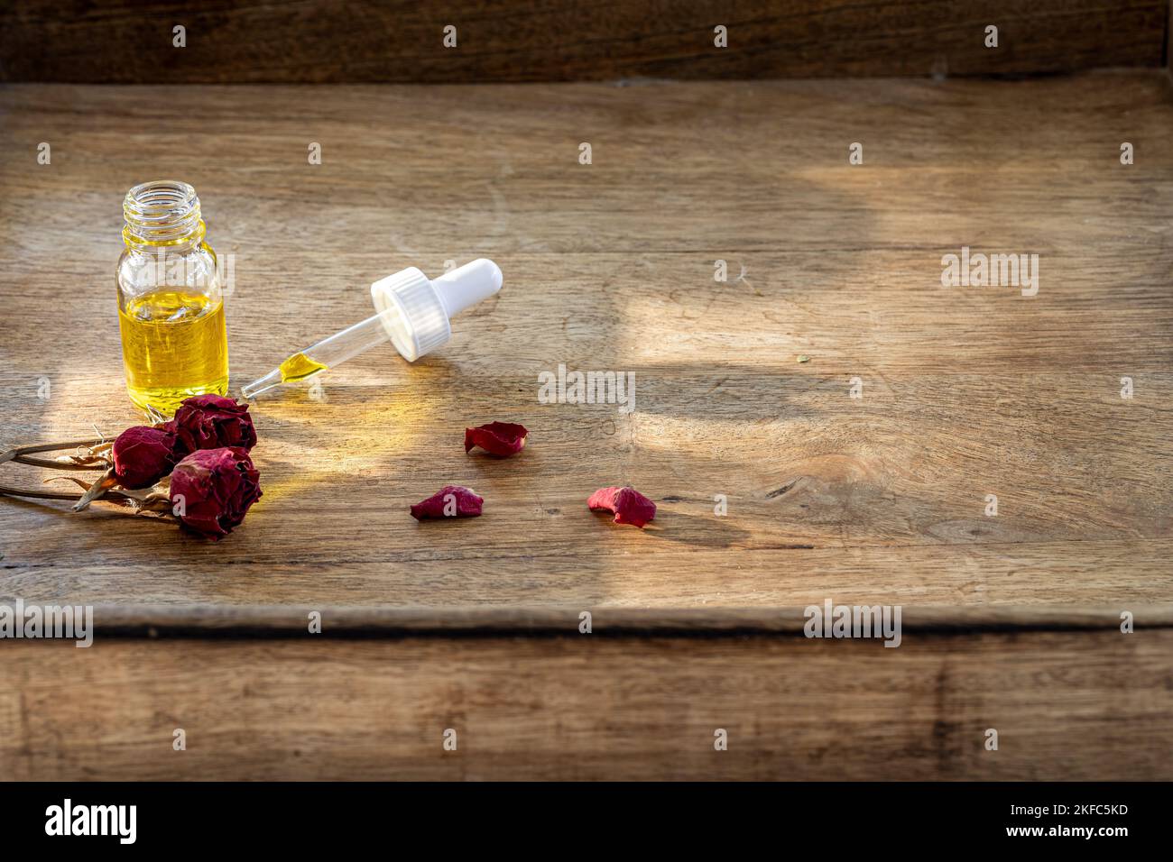 Olio essenziale in una piccola bottiglia di vetro con rose rosa essiccate in germoglio su uno sfondo di legno. Messa a fuoco selettiva e spazio di copia per il testo. Naturale cosmetica pro Foto Stock