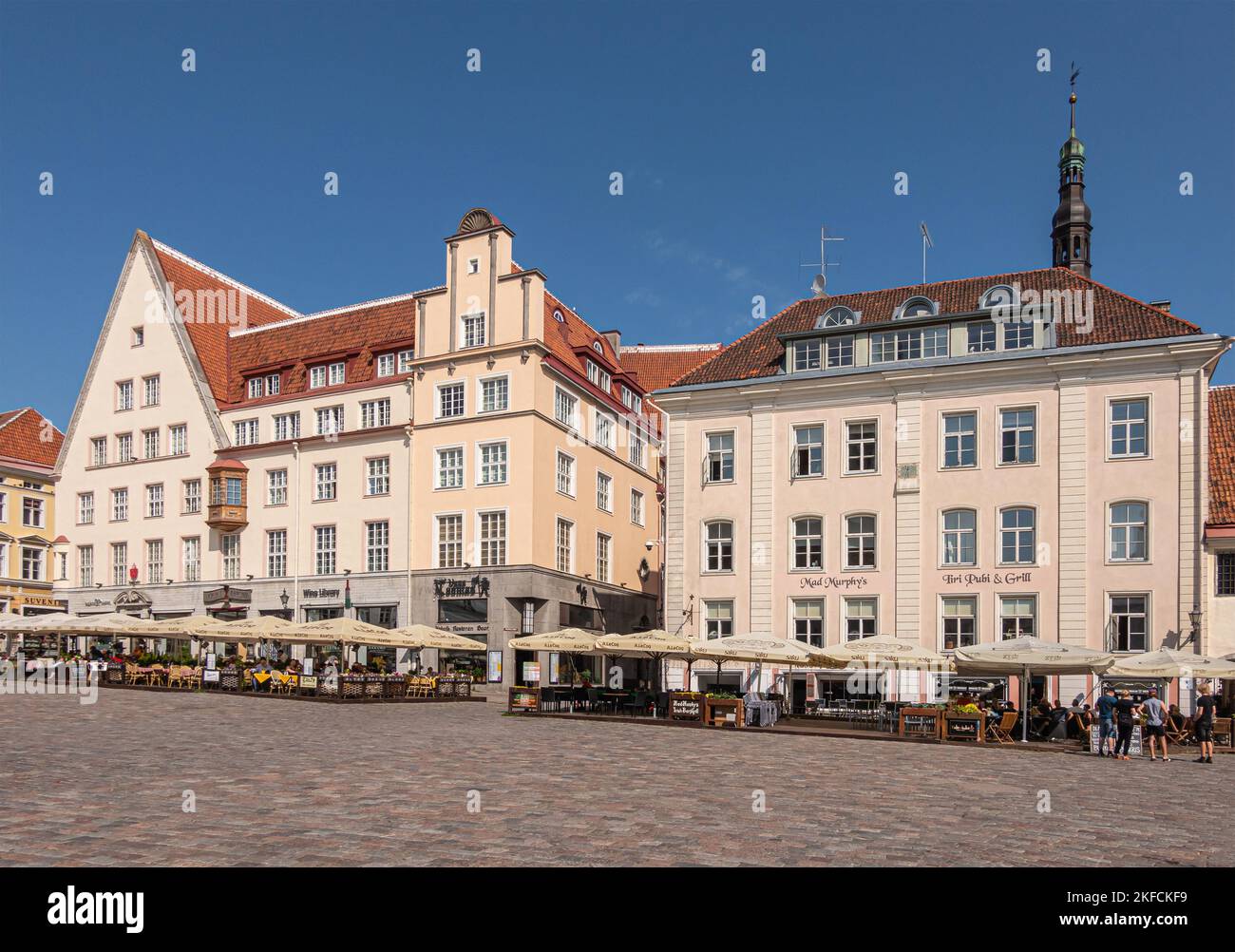 Estonia, Tallinn - 21 luglio 2022: Fila di ristoranti e pub sul lato nord della piazza del municipio offrono architettura moderna con facciate beige sotto blu Foto Stock